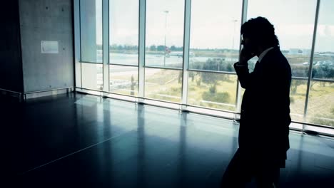 Businessman-walking-on-airport-corridor-and-talking-on-mobile-phone