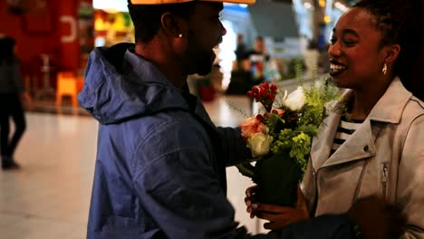 Junger-Mann,-umarmen-und-begrüßen-Frau-mit-Blumen-am-Flughafen