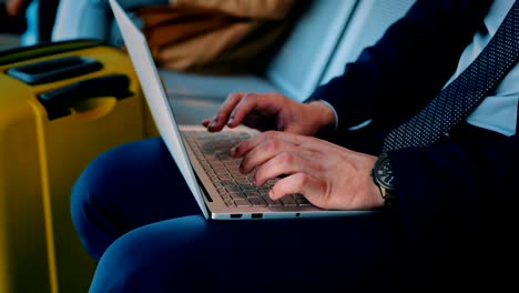 Businessman-typing-on-laptop-while-sitting-in-airport-waiting-room