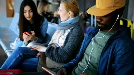 Multi-ethnic-travelers-sitting-on-bench-at-airport-gate