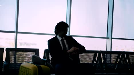 Businessman-sitting-on-bench-and-checking-the-time-at-airport