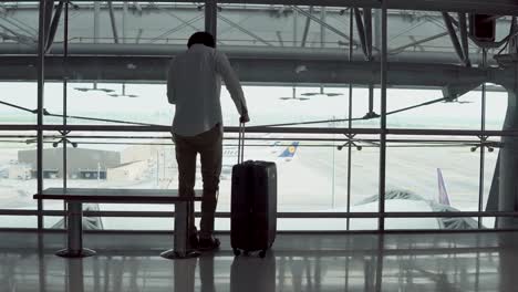 4K.-Male-Young-passenger-using-smartphone-walking-with-suitcase-luggage-and-sitting-on-bench-in-departure-area-of-airport-terminal.-Asian-businessman-on-business-trip.-Modern-travel-lifestyle-concepts