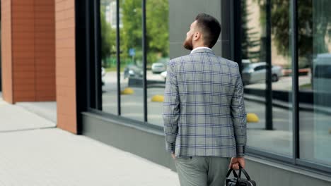 A-young-handsome-businessman-student-in-a-suit,-comes-with-a-briefcase,-at-the-station,-at-the-airport-or-business-center.-Rear-view