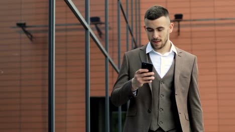 Man-using-business-app-on-smart-phone-walking-in-city.-Handsome-young-businessman-communicating-on-smartphone-smiling-confident