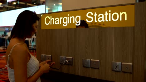 Eine-Frau-lädt-sich-ein-Smartphone-auf-die-Ladestation-am-Flughafen