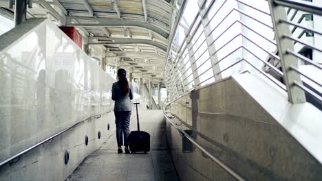 Asian-business-woman-talking-the-mobile-phone-while-dragging-a-wheeled-luggage-at-the-airport-ramp-for-business-trip