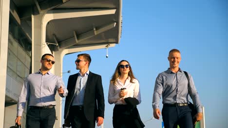 Group-of-young-happy-business-partners-walking-in-city-street-to-airport-terminal.-Colleagues-being-on-his-way-to-business-trip.-Portrait-of-smiling-business-people-stepping-and-talking.-Slow-motion-Close-up