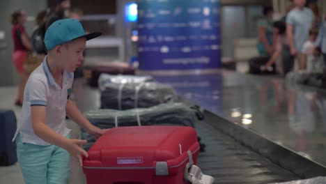 Boy-looking-for-his-suitcase-on-baggage-conveyor-belt-at-the-airport