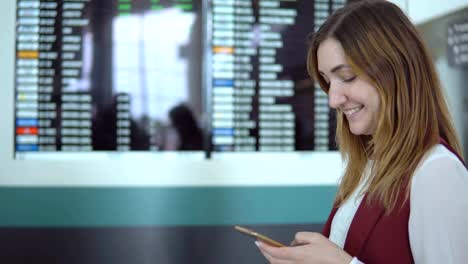 Pretty-girl-stands-on-the-background-of-blurry-scoreboard-with-the-notice-and-choice-flight-in-the-smartphone