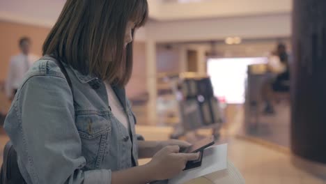 Gerne-Asiatin-mit-und-überprüfen-ihr-Smartphone-im-terminal-Halle-während-Sie-auf-ihren-Flug-am-Abfluggate-im-internationalen-Flughafen.-Frauen-glücklich-im-Flughafenkonzept.