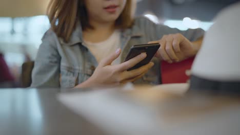 Feliz-mujer-asiática-utilizando-y-controlando-su-smartphone-sentado-en-silla-en-la-sala-terminal-mientras-espera-su-vuelo-en-la-puerta-de-salida-en-el-aeropuerto-internacional.-Mujer-feliz-en-concepto-de-aeropuerto.