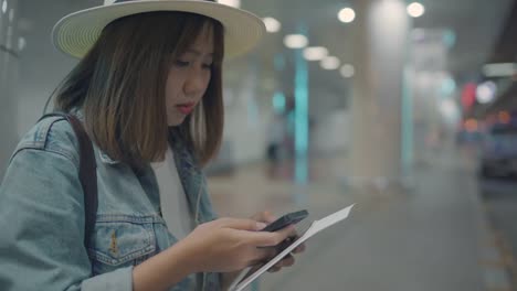 Feliz-mujer-asiática-utilizando-y-controlando-su-smartphone-en-el-hall-de-la-terminal-mientras-espera-su-vuelo-en-la-puerta-de-salida-en-el-aeropuerto-internacional.-Mujer-feliz-en-concepto-de-aeropuerto.