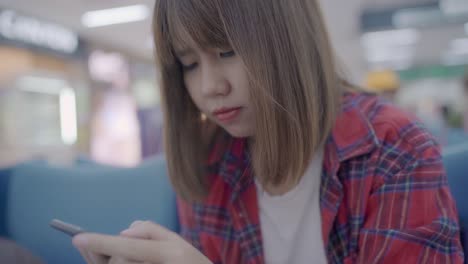 Happy-Asian-woman-using-and-checking-her-smartphone-while-sitting-on-chair-in-terminal-hall-while-waiting-her-flight-at-the-departure-gate-in-international-airport.-Women-happy-in-airport-concept.