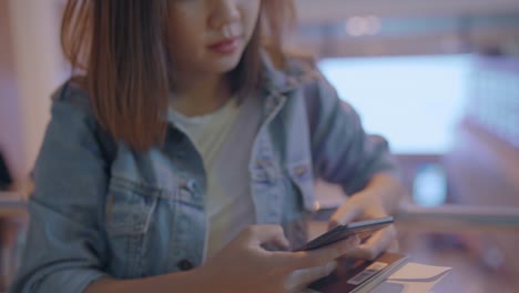 Feliz-mujer-asiática-utilizando-y-controlando-su-smartphone-en-el-hall-de-la-terminal-mientras-espera-su-vuelo-en-la-puerta-de-salida-en-el-aeropuerto-internacional.-Mujer-feliz-en-concepto-de-aeropuerto.