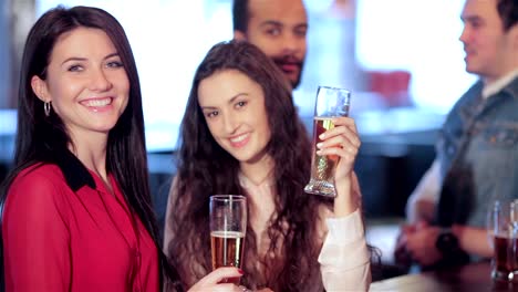 Two-cute-girls-standing-at-the-bar-are-talking-and-smiling-at-the-camera