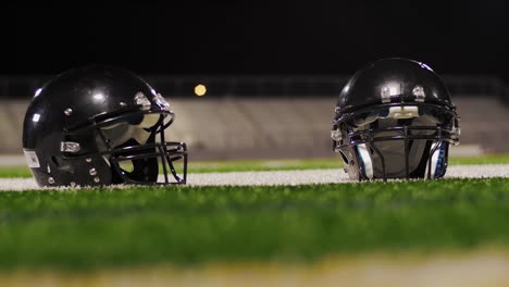 Close-up-of-two-football-helmets-on-the-field-with-players-walking-through-the-foreground