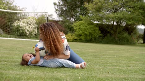 Chica-joven-acostado-sobre-hierba-con-pelota-jugando-con-su-madre