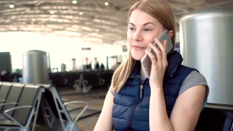 Beautiful-attractive-young-woman-using-smartphone-in-airport.-Talking-to-her-friend.-Smiling