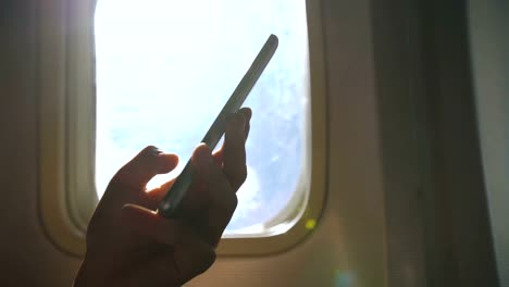 Closeup-of-woman-hands-sitting-near-airplane-window-using-mobile-phone-during-flight