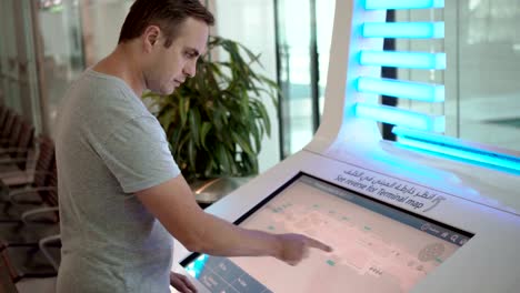 Serious-handsome-man-in-airport-terminal.-Using-touchscreen,-searching-for-flight-information