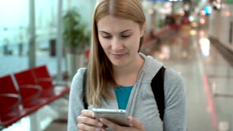 Frau-zu-Fuß-im-Flughafen-terminal.-Verwendung-von-Smartphone,-browsing,-messaging-mit-Freunden,-lesen-Nachrichten