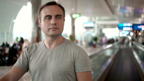 Handsome-young-man-in-airport-terminal.-Waiting-for-flight.-Using-travolator,-looking-around