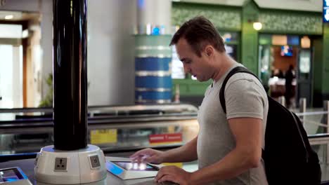 Hübscher-junger-Mann-im-Flughafen-terminal.-Stand-in-der-Nähe-der-Ladestation-mit-Touchscreen,-Surfen