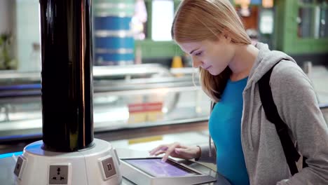 Beautiful-attractive-woman-in-airport-terminal.-Standing-near-charging-stand-using-touchscreen