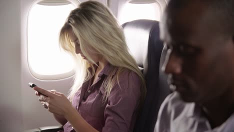 Young-woman-using-mobile-phone-on-airplane-flight
