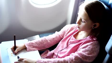 Adorable-little-girl-traveling-by-an-airplane.-Kid-drawing-picture-with-colorful-pencils-sitting-near-window