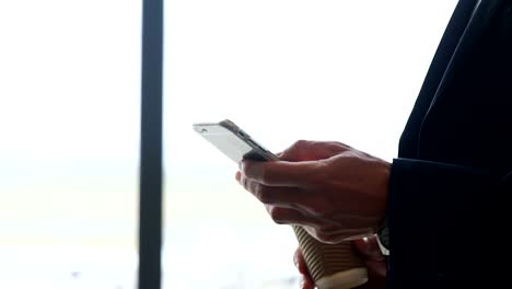 Businessman-holding-disposable-cup-texting-on-mobile-phone