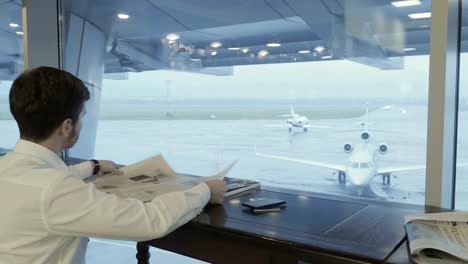 Cute-man-talks-on-the-phone-and-reads-the-newspaper-in-the-airport