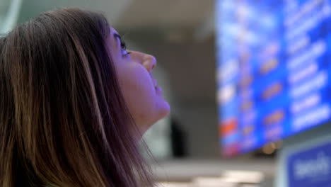 Junge-Frau-schaut-auf-der-Infotafel-der-Abflüge-am-Flughafen.