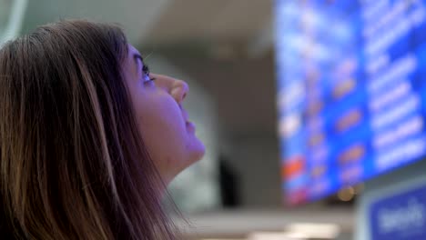 Junge-Frau-schaut-auf-der-Infotafel-der-Abflüge-am-Flughafen.