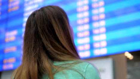 Mujer-joven-se-ve-en-el-tablero-de-información-de-las-salidas-en-el-aeropuerto.