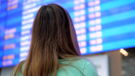 Junge-Frau-schaut-auf-der-Infotafel-der-Abflüge-am-Flughafen.