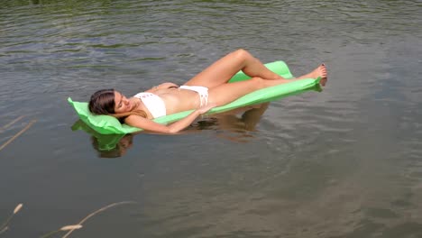 Jóvenes-bronceados-a-mujer-en-un-Bikini-blanco-flotando-en-el-río-sobre-el-colchón.