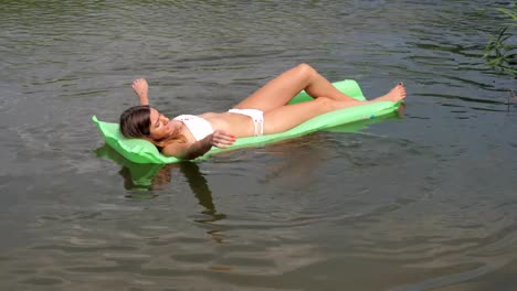 Junge-gebräunte-Frau-In-einem-weißen-Bikini-schwimmend-im-Fluss-auf-der-Matratze.