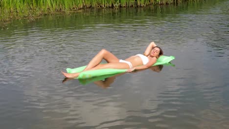 Pretty-Tanned-Woman-In-A-White-Bikini-Floating-In-The-River-On-The-Mattress.