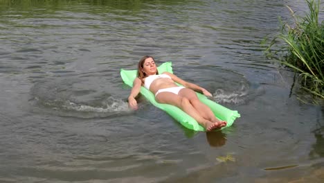 Junge-gebräunte-Frau-In-einem-weißen-Bikini-schwimmend-im-Fluss-auf-der-Matratze.