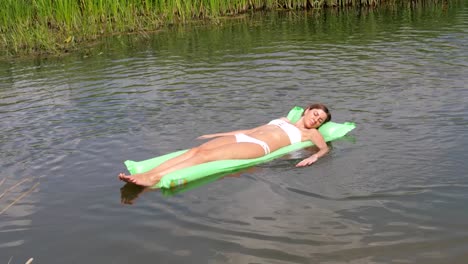 Schöne-gebräunte-Frau-In-einem-weißen-Bikini-schwimmend-im-Fluss-auf-der-Matratze.