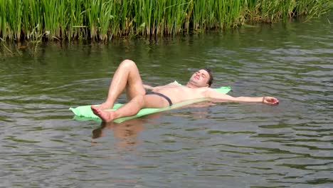 El-hombre-de-reclinación-en-el-caluroso-día-de-verano-de-natación-en-el-río-sobre-el-colchón.