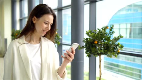 Portrait-of-young-woman-with-smartphone-in-international-airport.-Airline-passenger-in-an-airport-lounge-waiting-for-flight-aircraft