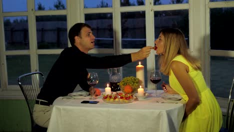 Lovely-Couple-Sits-in-the-Restaurant,-the-Man-Hand-Feed-His-Girlfriend-Canapes