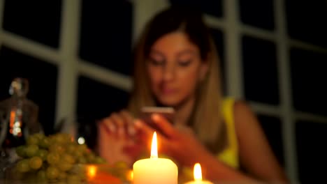Mujer-en-vestido-amarillo-cenando-en-el-restaurante-con-velas-usa-Smartphone