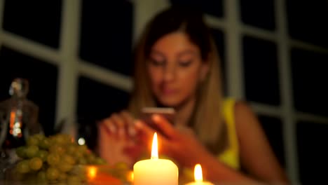 Frau-im-gelben-Kleid-mit-Abendessen-im-Restaurant-bei-Kerzenlicht-nutzt-Smartphone