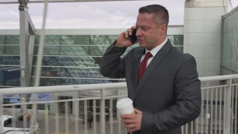 Businessman-walking-and-talking-on-cell-phone-at-airport