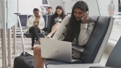 Mujer-hablando-por-teléfono-celular-usando-un-ordenador-portátil-en-el-aeropuerto