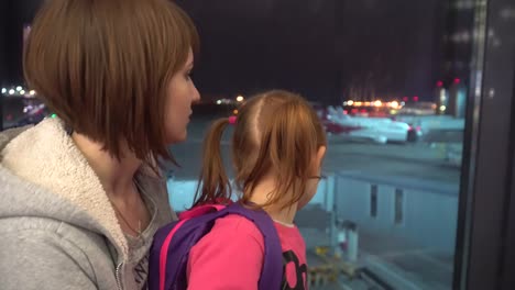 Una-pequeña-niña-con-mamá-mira-los-aviones-en-el-aeropuerto