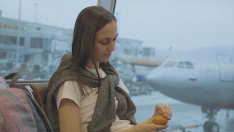 Joven-come-mandarina-en-el-aeropuerto-con-el-avión-en-el-fondo